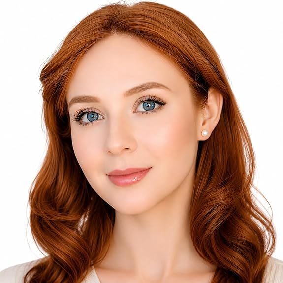 A red headed woman with blue eyes wears pearl earrings with lipstick and makeup on her face.