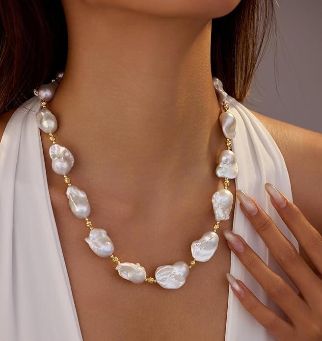 A woman in a white dress wears a chunky pearl necklace with real big pearls and a gold lined chain.
