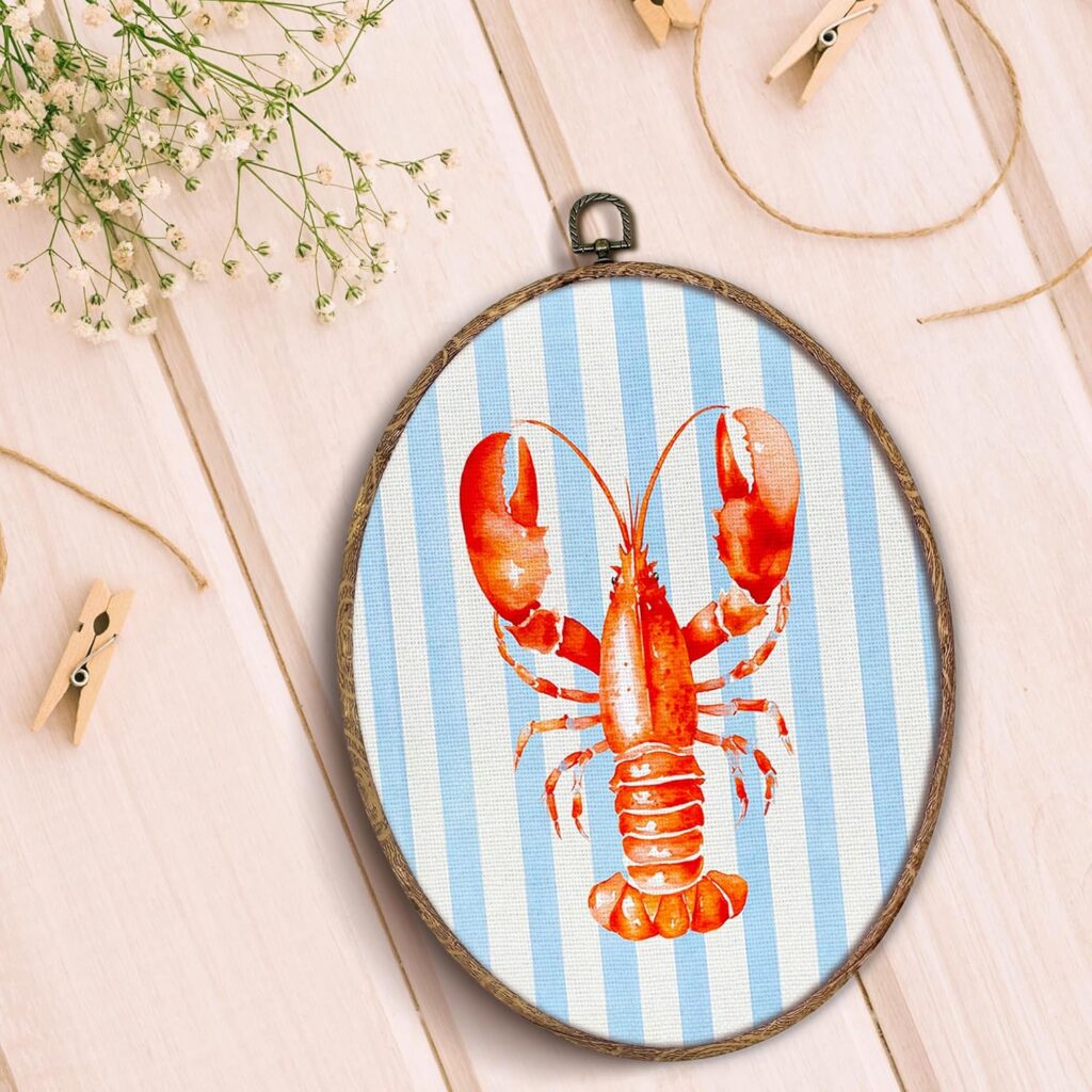 A oval wall art piece with blue and white horizontal stripes and a red lobster on it. Nautical home decoration.